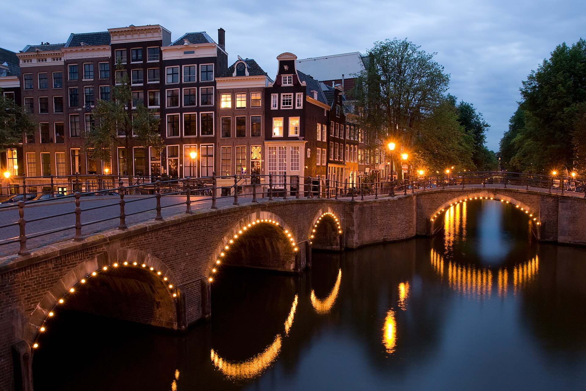 Canal bridges strung with lights at dusk in Amsterdam