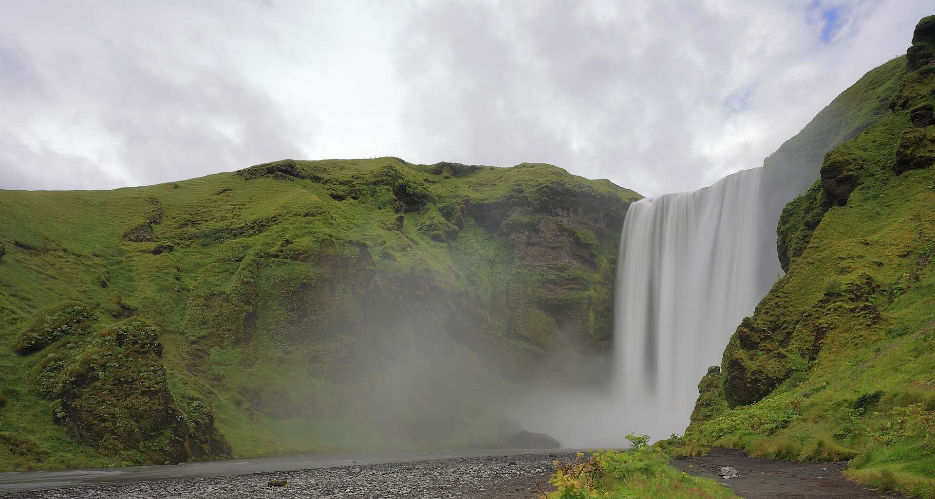 The Skógafoss waterfall falling between green cliffs