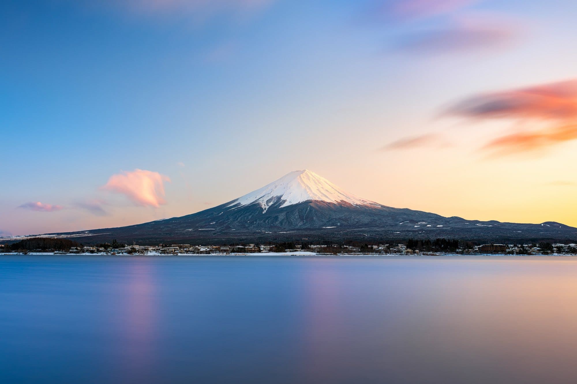 Snow-capped Mount Fuji at sunset, reflected in a still lake