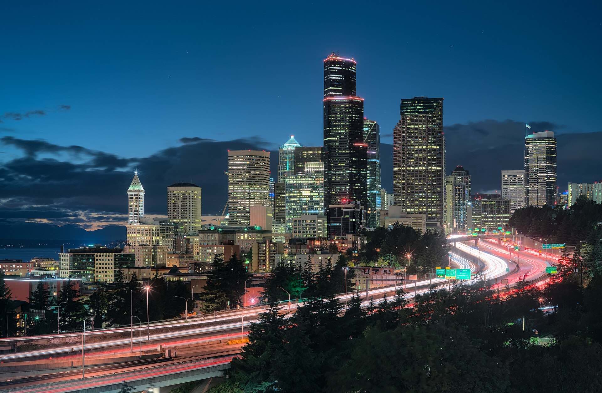 The Seattle skyline at dusk above streaks of highway lights