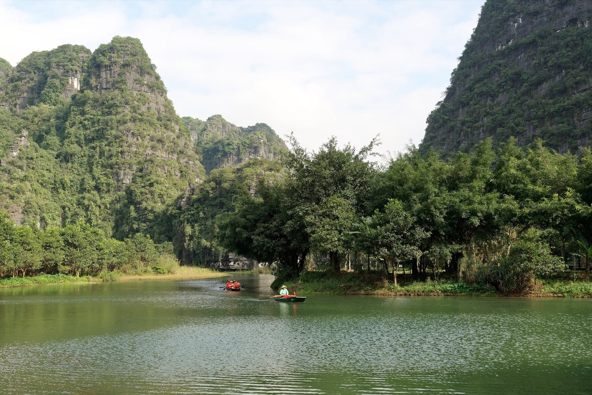 A small rowing boat on a river between forested limestone cliffs